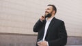 Young bearded business man talking on cell phone making deals with cup of coffee near modern office buildings Royalty Free Stock Photo