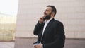 Young bearded business man talking on cell phone making deals with cup of coffee near modern office buildings Royalty Free Stock Photo