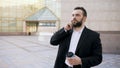 Young bearded business man talking at smartphone with cup of coffee near office buildings outdoors Royalty Free Stock Photo