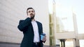 Young bearded business man talking at smartphone with cup of coffee near office buildings outdoors Royalty Free Stock Photo