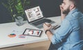 Young bearded businessman in denim shirt is sitting at office at table, talking on mobile phone and drinking coffee. Royalty Free Stock Photo