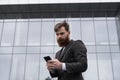 Young bearded Businessman holding mobile smartphone using app texting sms message wearing jacket outdoor. Successful Royalty Free Stock Photo