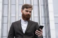 Young bearded Businessman holding mobile smartphone using app texting sms message wearing jacket outdoor. Successful Royalty Free Stock Photo