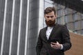 Young bearded Businessman holding mobile smartphone using app texting sms message wearing jacket outdoor. Successful Royalty Free Stock Photo