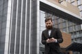 Young bearded Businessman holding mobile smartphone using app texting sms message wearing jacket outdoor. Successful Royalty Free Stock Photo