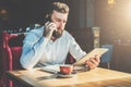 Young bearded businessman sits in cafe at table, talking on mobile phone, holding tablet computer.Man is working Royalty Free Stock Photo