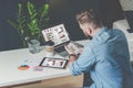 Young bearded businessman sits in office at table and uses smartphone with charts,diagrams and graphs on screen. Royalty Free Stock Photo