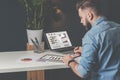 Young bearded businessman sits in office at table,using digital tablet and explores charts,making notes. Royalty Free Stock Photo