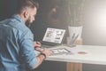 Young bearded businessman sits in office at table,using tablet computer and explores charts,making notes. Royalty Free Stock Photo