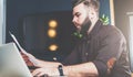 Young bearded businessman sitting in office at table, reading documents and working on laptop. Man blogging, chatting Royalty Free Stock Photo