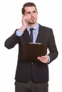 Young bearded businessman in suit using phone and holding clipboard Royalty Free Stock Photo