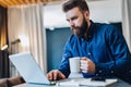 Young bearded businessman working on computer at table, drinking coffee.Man analyzes information, develops business plan