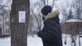 Young bearded Caucasian man talking on the phone and looking at missing person ad hanging on the tree. Empathic guy in