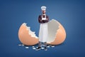 A young bearded cook in a white apron and a hat stands near a large broken egg shell.