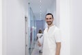 Portrait of a Young smiling bearded doctor holding a folder while leaning on white wall and looking to camera at a clinic corridor Royalty Free Stock Photo