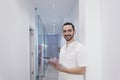 Portrait of a Young smiling bearded doctor holding a folder while leaning on white wall and looking to camera at a clinic corridor Royalty Free Stock Photo