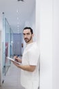 Portrait of a Young smiling bearded doctor holding a folder while leaning on white wall and looking to camera at a clinic corridor Royalty Free Stock Photo