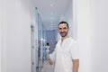 Portrait of a Young smiling bearded doctor holding a folder while leaning on white wall and looking to camera at a clinic corridor Royalty Free Stock Photo