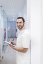 Portrait of a Young smiling bearded doctor holding a folder while leaning on white wall and looking to camera at a clinic corridor Royalty Free Stock Photo