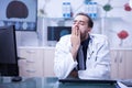 Young bearded doctor tired and yawning sitting at the office in his hospital cabinet Royalty Free Stock Photo