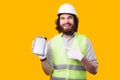 A young bearded engineer smiling at the camera is showing a brand new tablet near a yellow wall Royalty Free Stock Photo