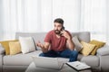 Young bearded freelancer expert business man sitting on the sofa talking on the phone and working on his laptop with his boss Royalty Free Stock Photo