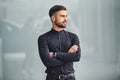 Young bearded guy in elegant clothes standing indoors against grey background Royalty Free Stock Photo