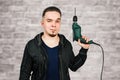 Young bearded guy holding drill on brick wall background