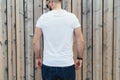 Young bearded hipster man dressed in white t-shirt and sunglasses is stands outdoor against wood wall. Mock up. Royalty Free Stock Photo