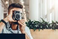 Young bearded man sits in coffee shop at table in front of laptop and takes instant photo on camera. Royalty Free Stock Photo