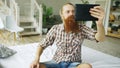 Young bearded man using tablet computer having video chat sitting in bed at home Royalty Free Stock Photo