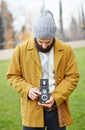 Young bearded hipster taking photo with TLR camera