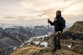 Young bearded hipster wearing a hat and sunglasses with Nordic walking sticks and a backpack moves in the mountains at