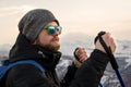 Young bearded hipster wearing a hat and sunglasses with Nordic walking sticks and a backpack moves in the mountains at