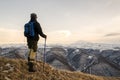 Young bearded hipster wearing a hat and sunglasses with Nordic walking sticks and a backpack moves in the mountains at