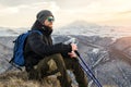 Young bearded hipster wearing a hat and sunglasses with Nordic walking sticks and a backpack moves in the mountains at