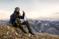 Young bearded hipster wearing a hat and sunglasses with Nordic walking sticks and a backpack moves in the mountains at