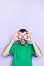 Young man holding slices of red onion in front of his eyes