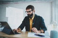 Young bearded male architect wearing eye glasses working on a digital tablet dock at his desk. Professional experienced Royalty Free Stock Photo
