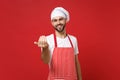 Young bearded male chef cook or baker man in striped apron white t-shirt toque chefs hat posing isolated on red Royalty Free Stock Photo