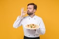 Young bearded male chef cook or baker man in white uniform shirt isolated on yellow background. Cooking food concept Royalty Free Stock Photo