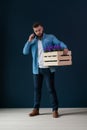Young bearded male hipster, dressed in denim shirt, stands indoors holding wooden box with flowers Royalty Free Stock Photo