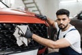 Young bearded male professional car wash worker, holding the gray microfiber and wiping grille