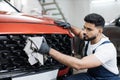 Young bearded male professional car wash worker, holding the gray microfiber and wiping grille