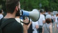 Young bearded male protester with megaphone bullhorn marches and talks on street