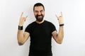 Young bearded man, black t-shirt and tattoos on an  white background, shouts with crazy expression doing the rock sibble w Royalty Free Stock Photo