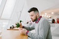 Young bearded man in cafe. He dressed in gray pullover and plaid shirt. Man holds tea and looks at smartphone