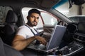 Young bearded man car technician mechanic sitting inside red car repairing problem of engine Royalty Free Stock Photo