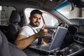 Young bearded man car technician mechanic sitting inside red car repairing problem of engine