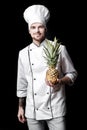 Young bearded man chef In white uniform holds Fresh pineapple on black background Royalty Free Stock Photo